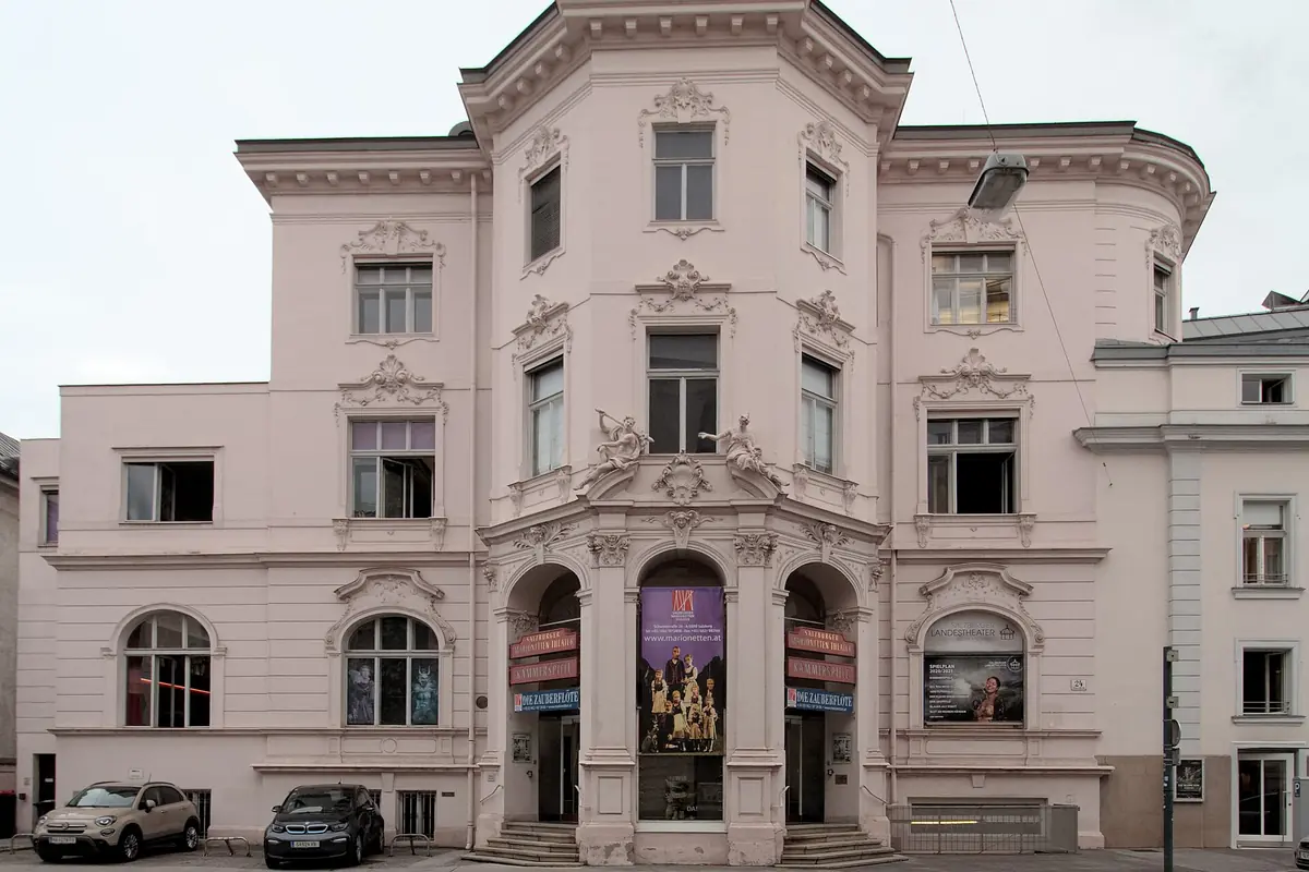 The pale pink Baroque-style facade of the theatre building on Schwarzstraße, with three arched entrance doors and a mansard roof