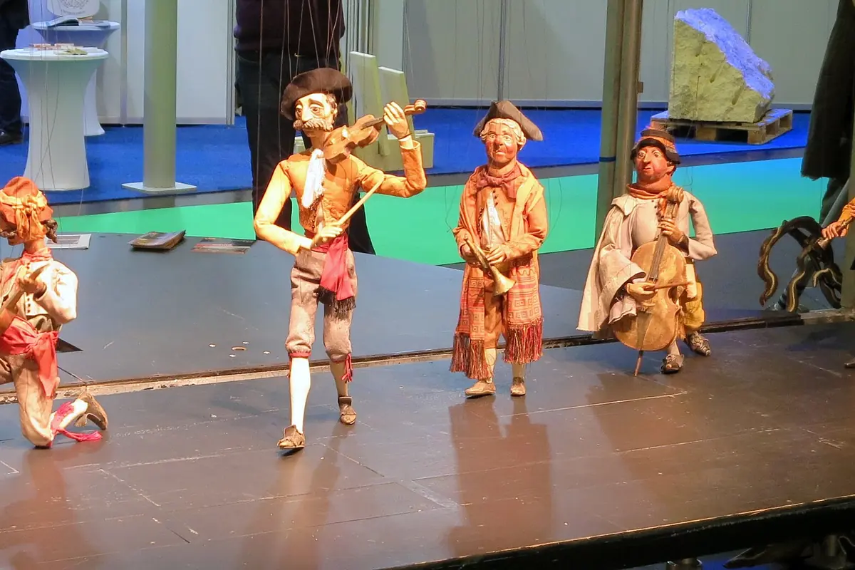 Marionette musicians in eighteenth-century costume, including a violinist, stand on a stage with strings above them